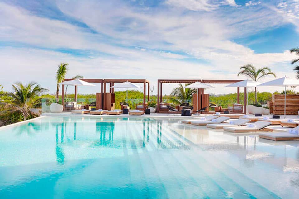 Luxury infinity pool with turquoise water and wooden sun loungers under pergola structures