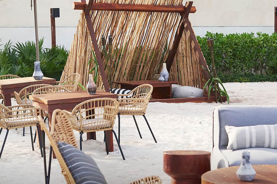 Beachside lounge with woven chairs, wooden pergola, and cabanas
