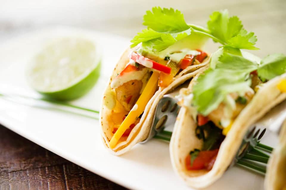 Colorful fish tacos with fresh cilantro garnish and lime wedge served on white plate