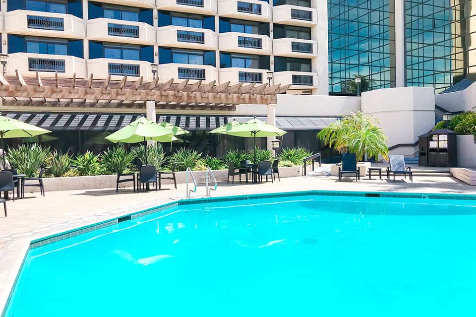Resort pool with bright turquoise water, lounge chairs, lime umbrellas, and high-rise hotel