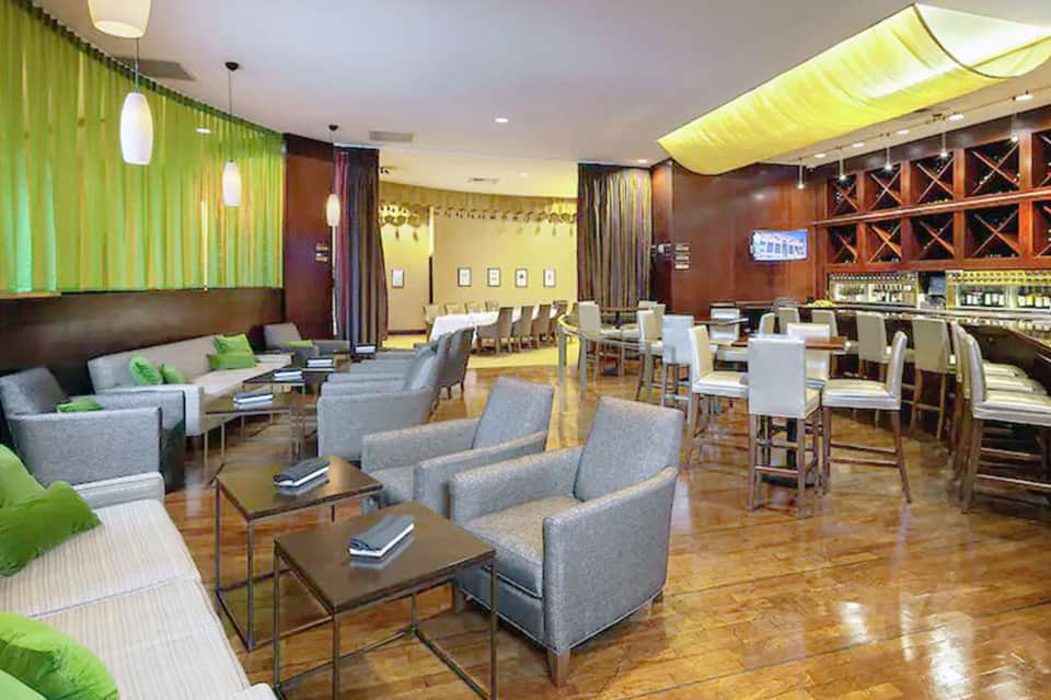 Modern hotel lounge with green accent walls, gray seating, and bar area with wood paneling