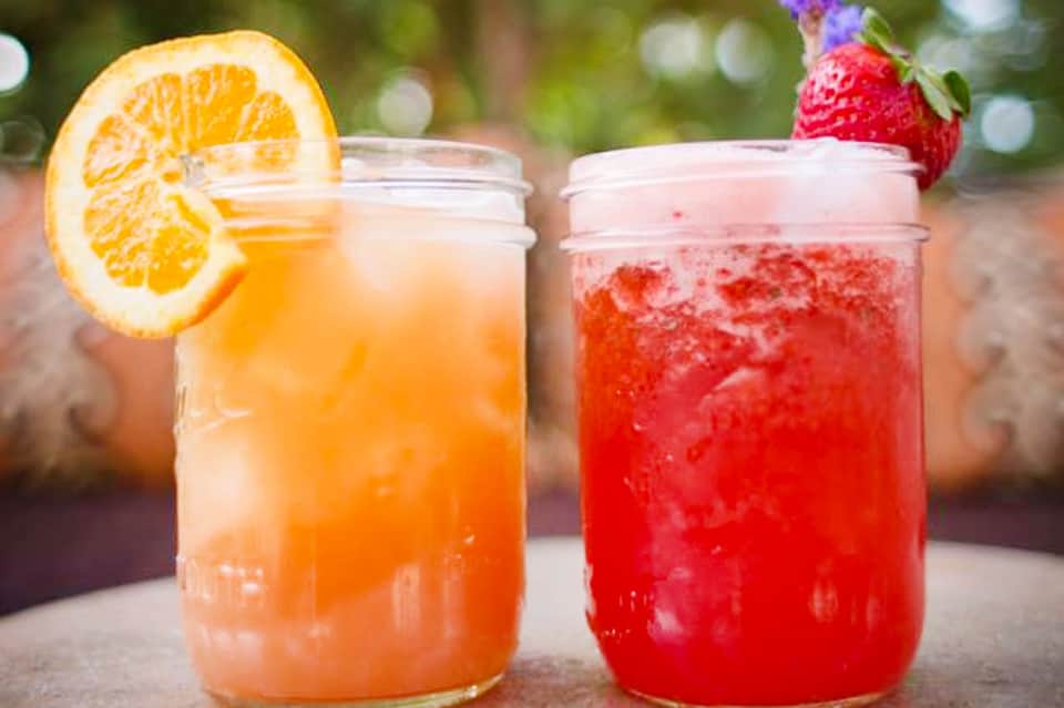 Two refreshing citrus and strawberry cocktails with ice and fresh fruit garnishes on outdoor table