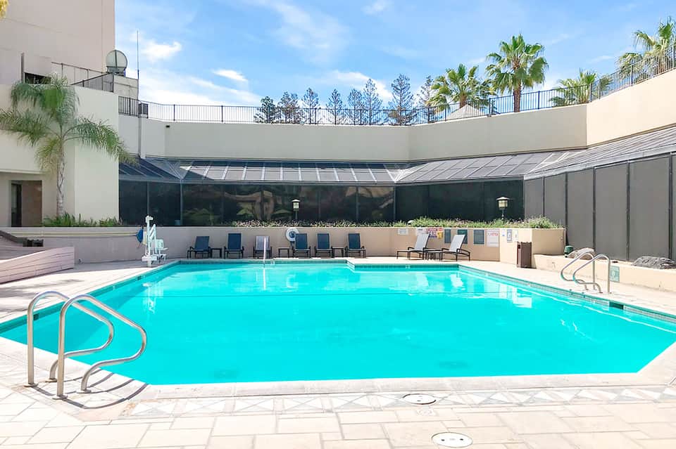 Indoor swimming pool with bright turquoise water, lounge chairs, and large windows overlooking palm trees