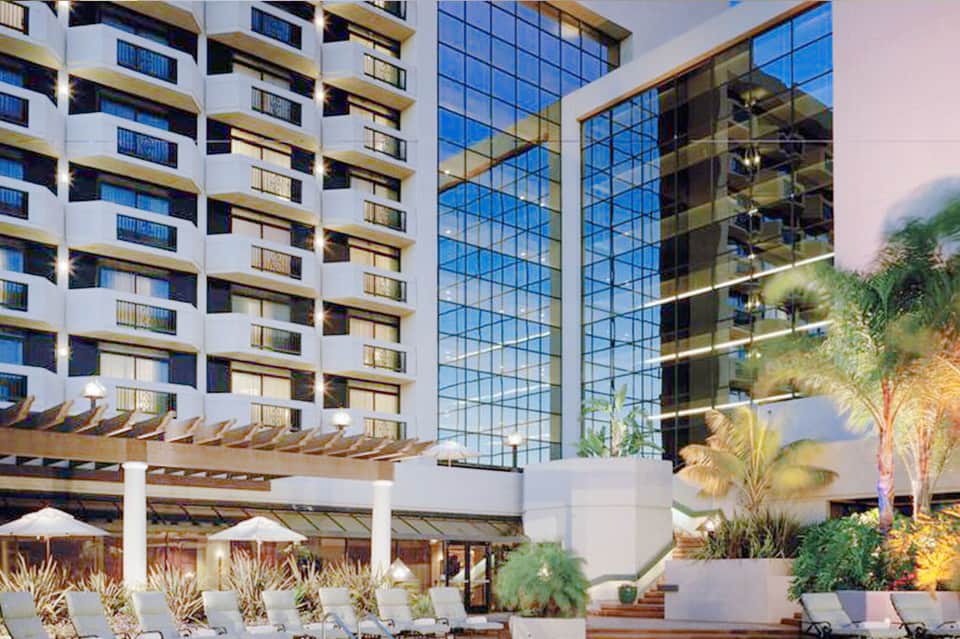 Modern hotel exterior with white buildings, glass atrium, pergolas, and illuminated landscaping at dusk