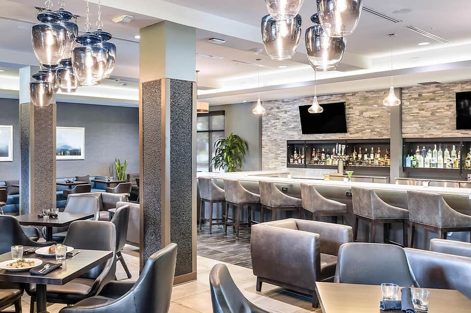 Upscale hotel bar and lounge with pendant lights, gray seating, and backlit bottles