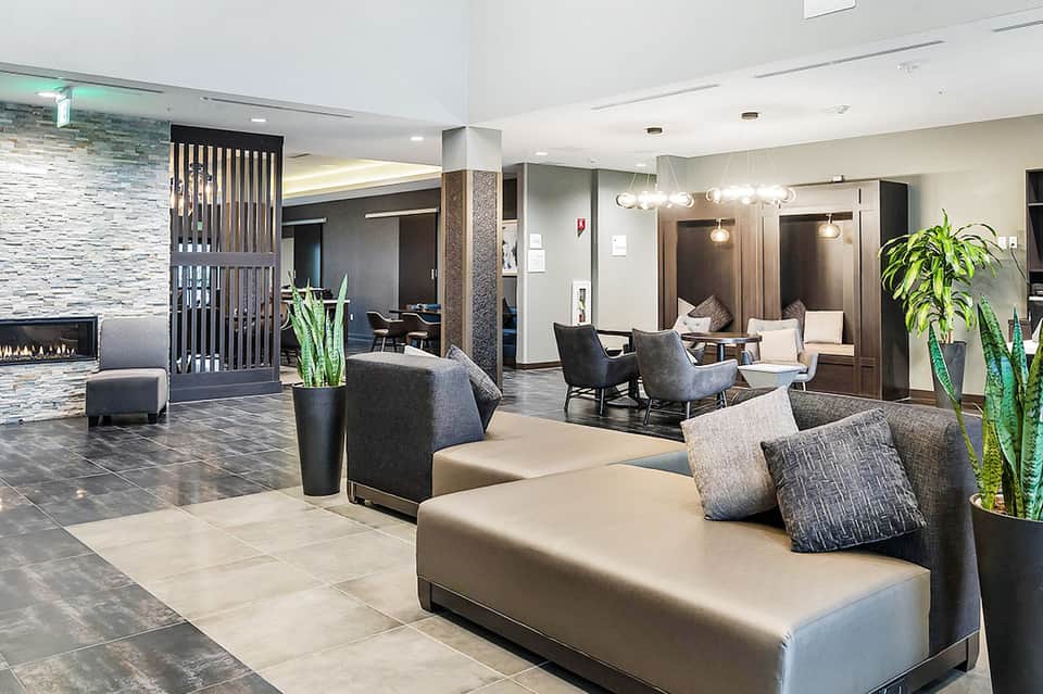 Contemporary hotel lobby featuring neutral tones, fireplace, modern furniture, and indoor plants