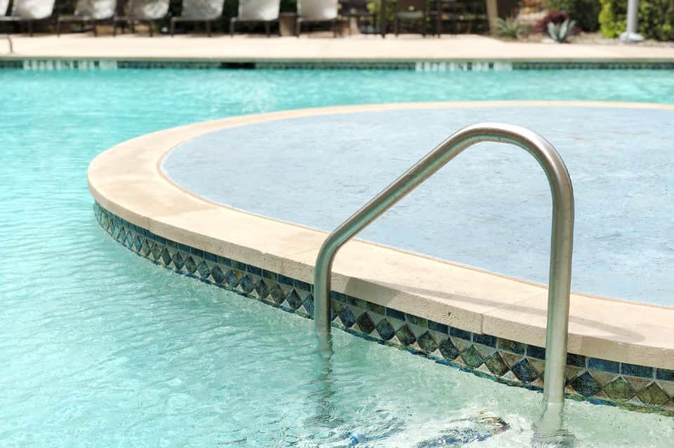 Pool handrail and curved deck edge with turquoise water and loungers