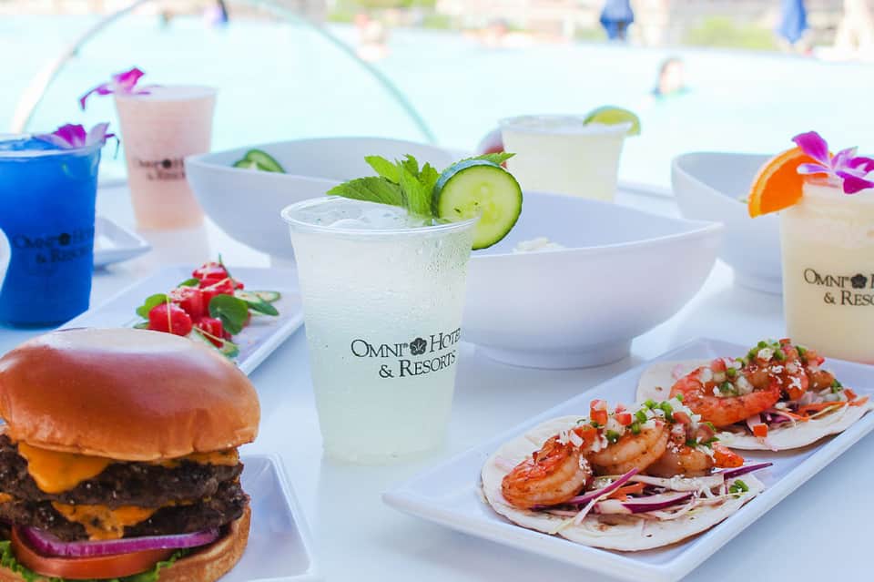 Gourmet food and beverage spread with cocktails, burger, and shrimp tacos at beachside venue