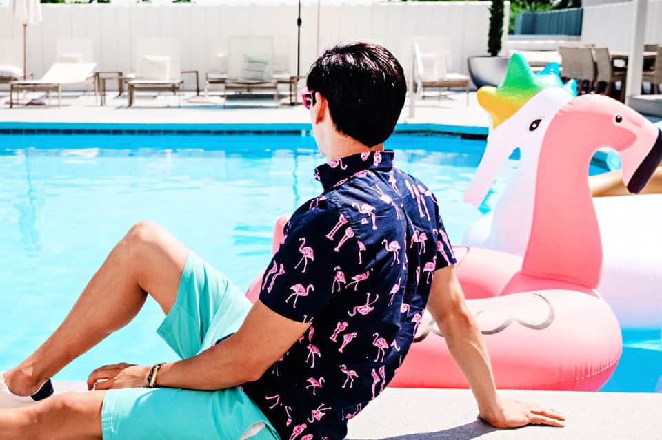 Man relaxing poolside on inflatable unicorn float in swim trunks