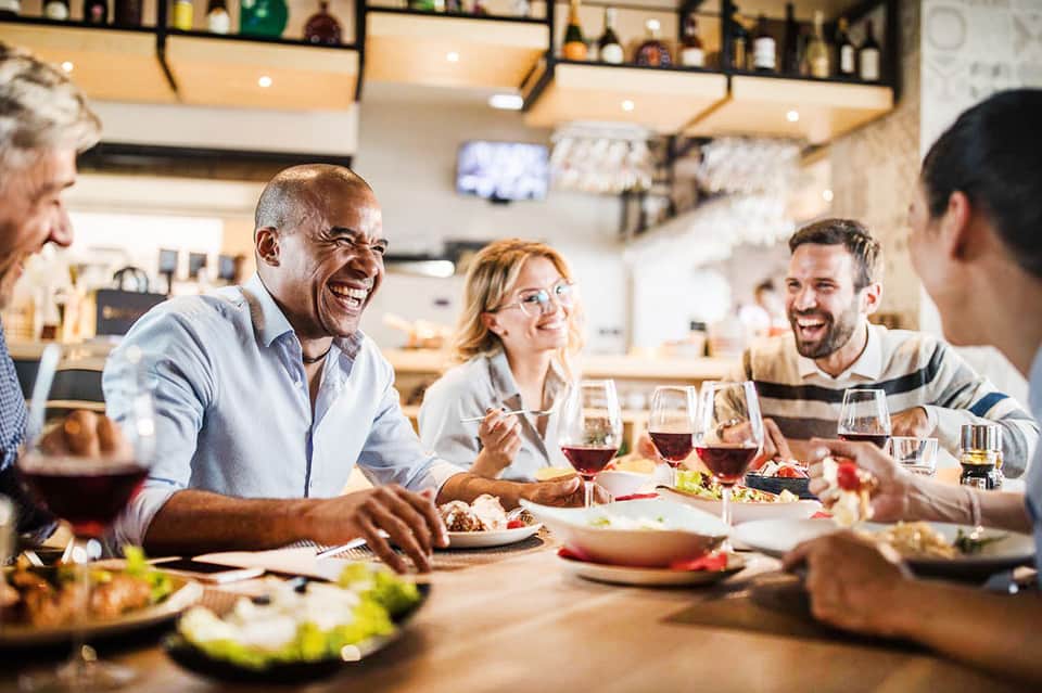 Group of people dining together at modern restaurant with wine glasses and plated food