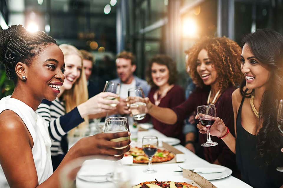 Friends toasting with wine glasses at indoor dinner party with food and smiles