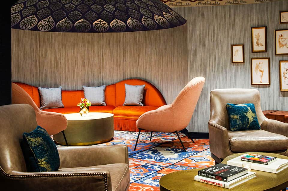 Upscale lounge with orange sofa, beige armchairs, patterned ceiling, and decorative artwork on walls
