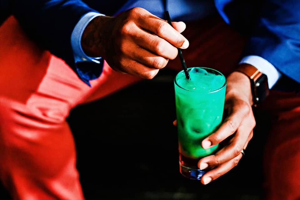 Person in formal attire holding bright green cocktail with straw