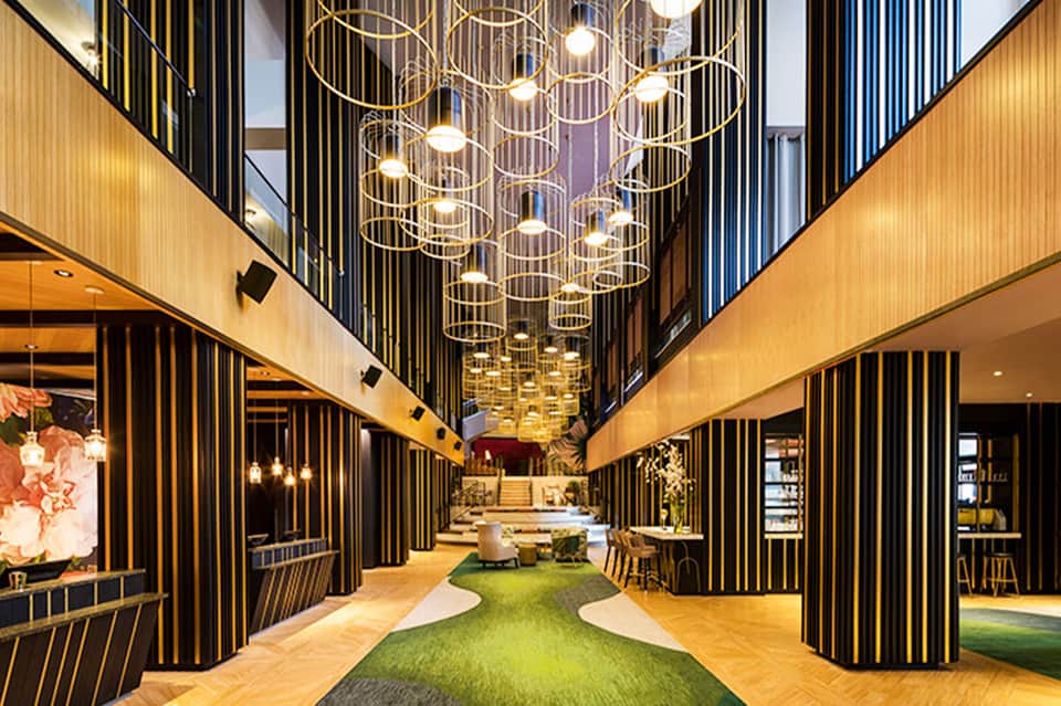 Contemporary hotel corridor with black and gold vertical stripe walls, artistic pendant lights, and green carpet accent