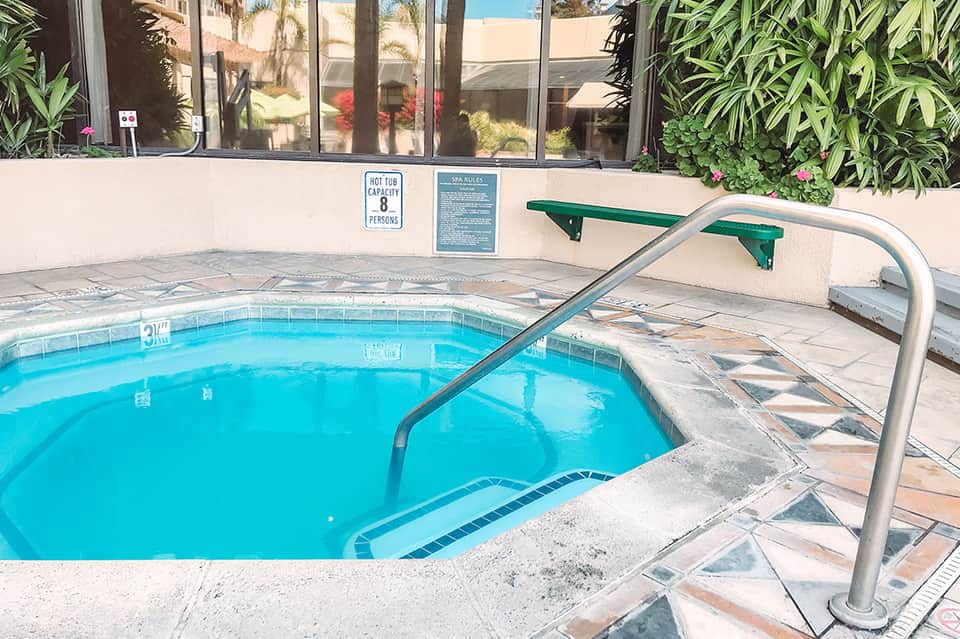 Spa hot tub with metal handrail and capacity sign, surrounded by desert landscape and modern building