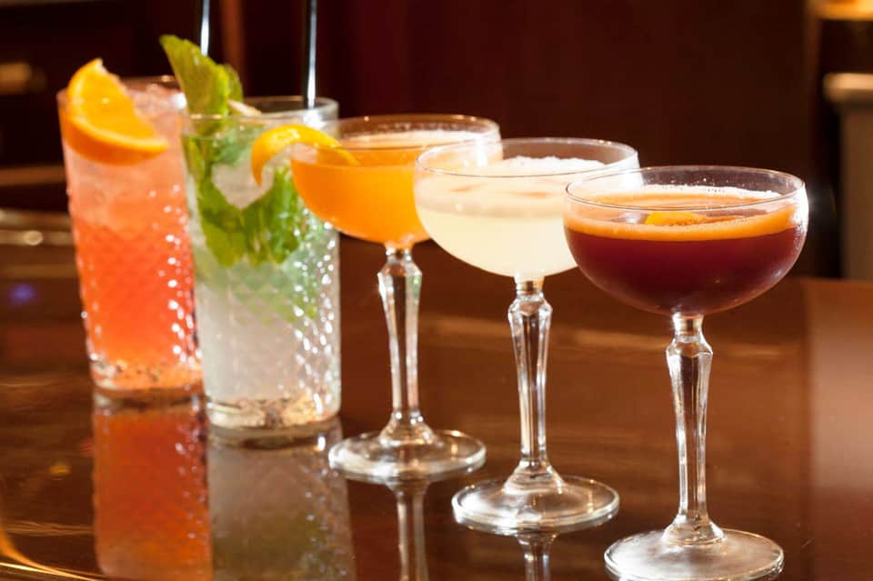 Four colorful cocktails on bar counter: coral, mint mojito, orange, and dark rum cocktail
