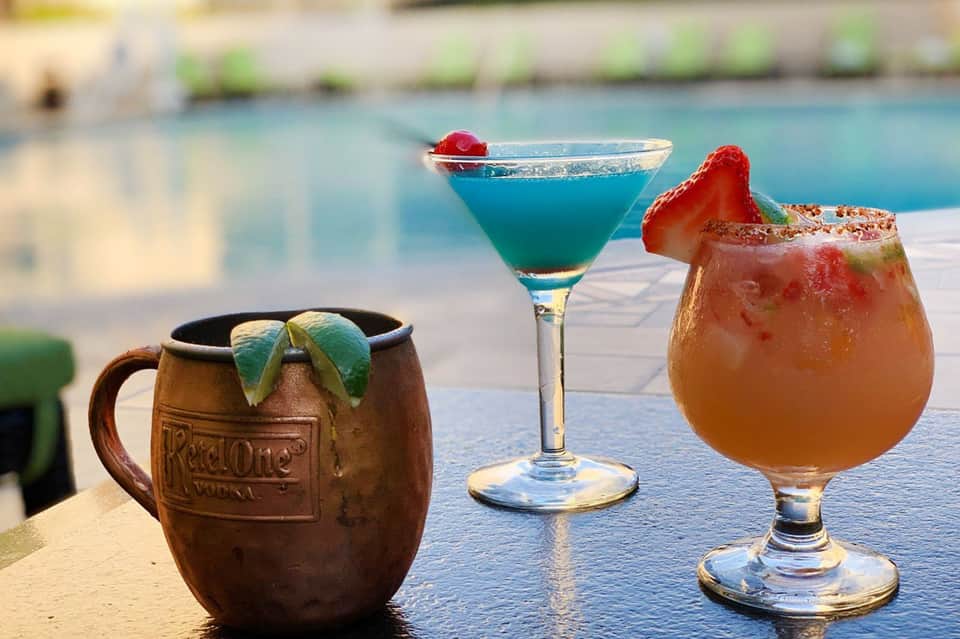 Three tropical cocktails displayed poolside: blue martini, rum mug, and fruity punch