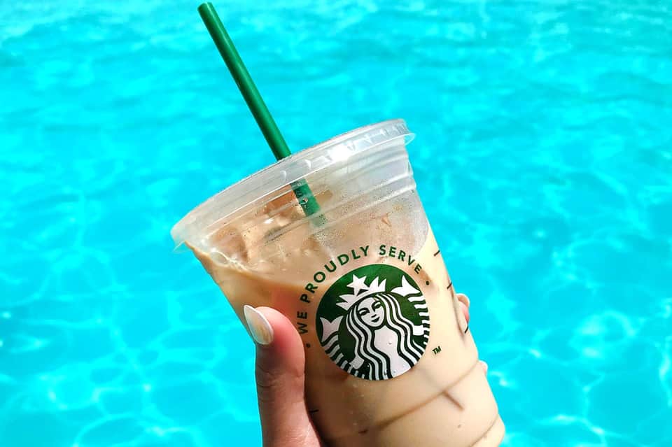 Iced coffee drink with Starbucks logo held above turquoise pool water