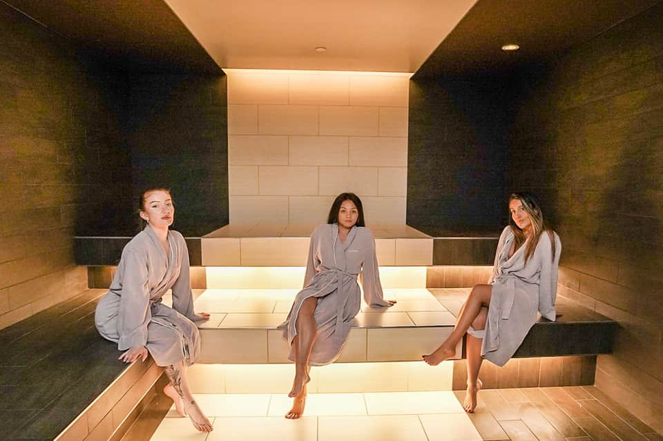 Three women in robes relaxing on heated stone benches in modern spa sauna
