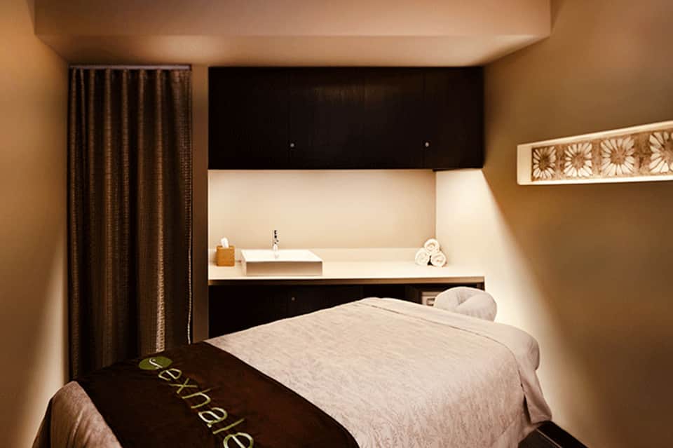 Spa massage room with modern design, dark headboard, bed, and sleek bathroom alcove