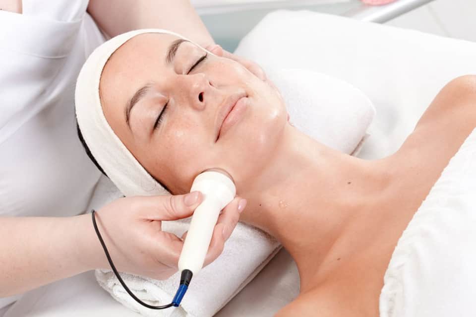 Woman receiving facial treatment with handheld spa device at luxury wellness center
