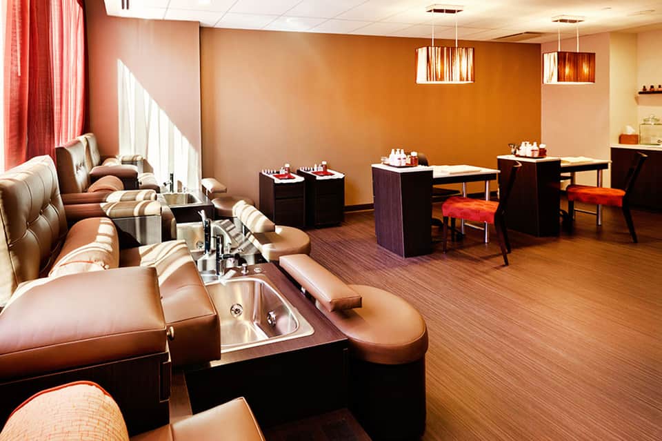 Spa salon interior with orange walls, pedicure stations, massage chairs, and modern lighting fixtures