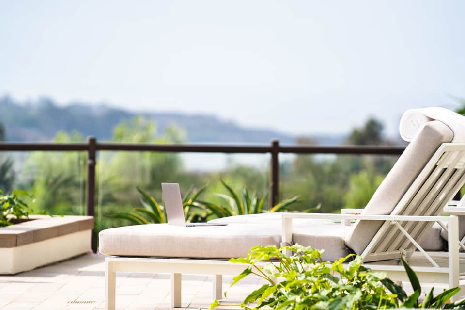 Modern lounge chairs and daybed on a sunny terrace with mountain views and flowering plants