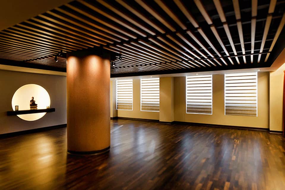 Modern interior space with black slatted ceiling, wooden flooring, and white horizontal shutter window treatments