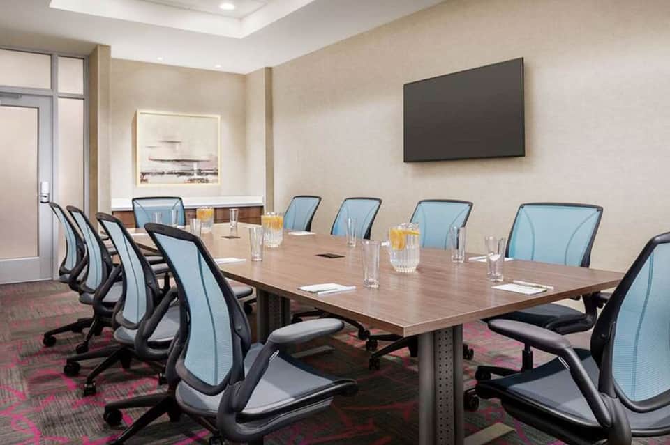 Modern conference room with wooden table, ergonomic blue chairs, wall-mounted TV, and professional setup