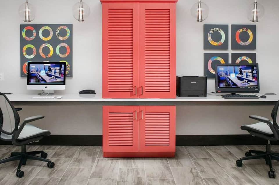 Modern office with dual workstations, red louvered storage cabinet, pendant lights, and colorful wall art