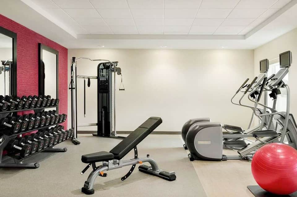 Modern fitness center with dumbbells, weight machines, exercise bikes, and red stability ball