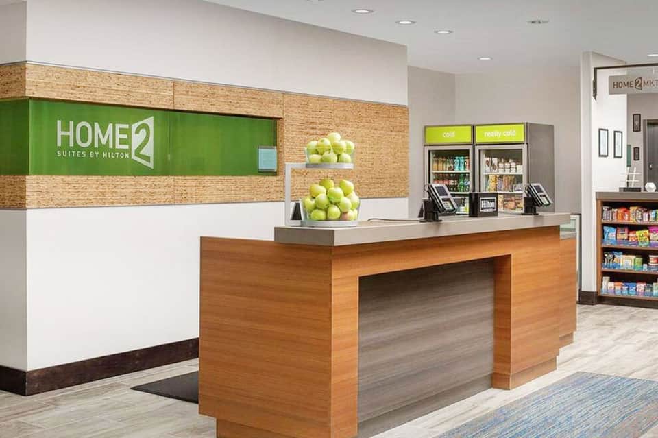 Home2 Suites hotel front desk with green signage, wooden reception counter, and merchandise displays