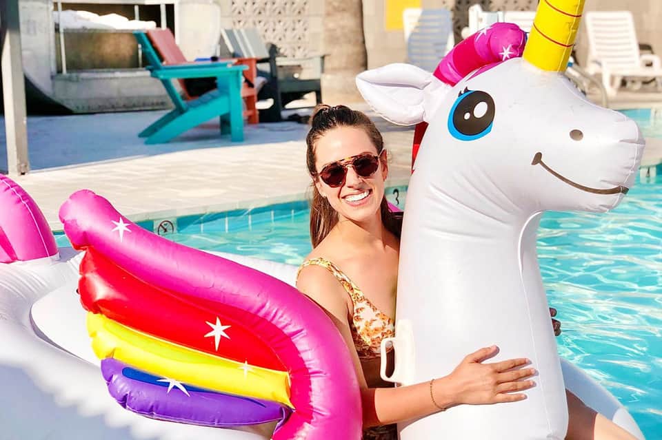 Woman in pool with colorful pool float and white unicorn inflatable