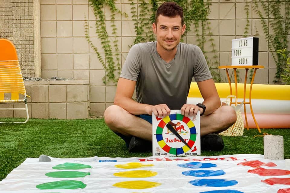 Man holding Twister game mat in modern backyard with artificial grass and contemporary furniture