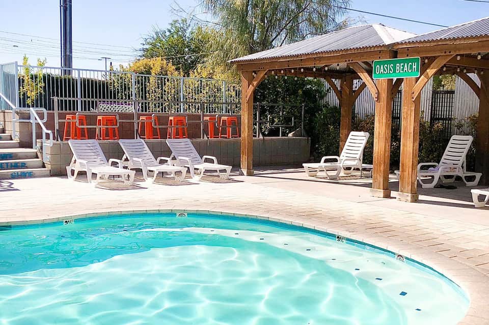 Resort pool with wooden pergola, white lounge chairs, and Oasis Beach sign