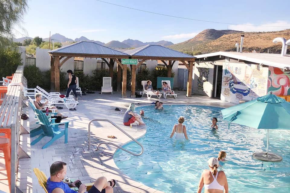 Casual pool area with families swimming, wooden pergola, and desert mountains