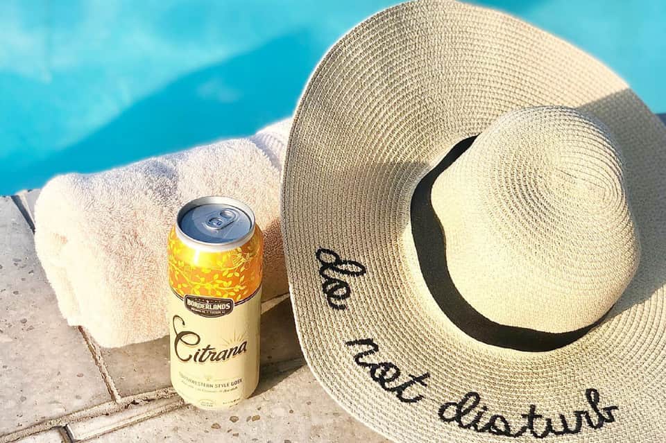 Poolside relaxation scene with straw hat, towel, and beverage on concrete deck