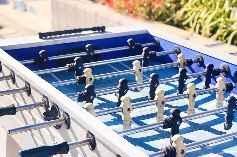 Foosball game table outdoors in sunny setting with colorful garden background