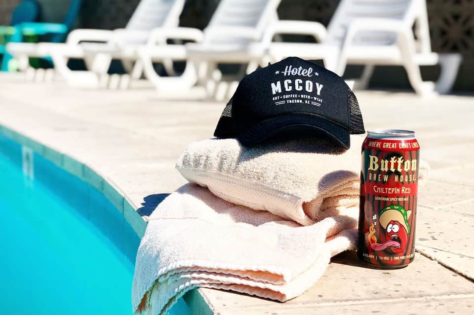Poolside scene at Hotel McCoy with towels, black cap, and Buttface Brew House beer can by the water.