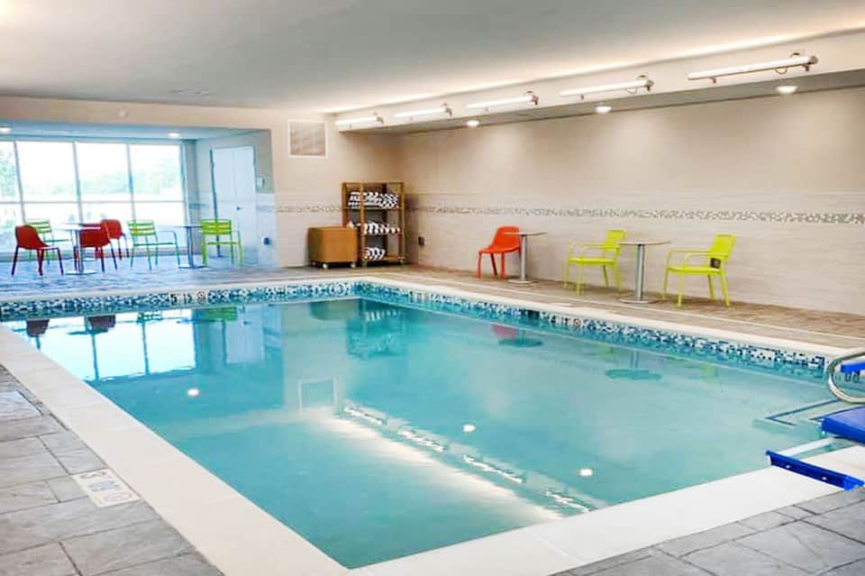 Indoor lap pool with turquoise water, lane markers, and colorful modern chairs