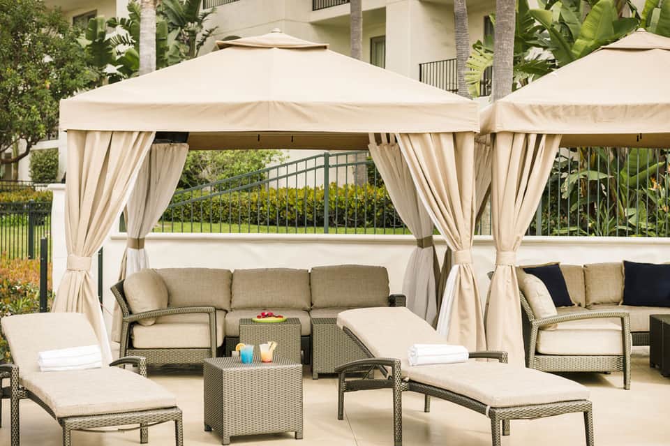 Luxury poolside cabanas with cream-colored gazebos, wicker seating, and curtains in an upscale resort setting