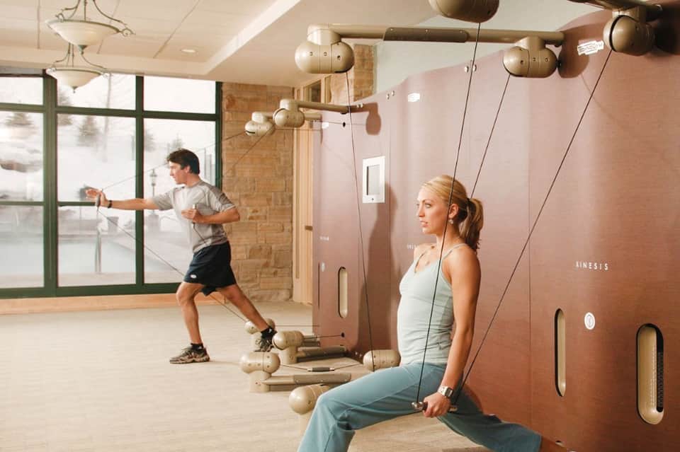 Modern fitness center with two people using cable machines, large windows, and pendant lighting