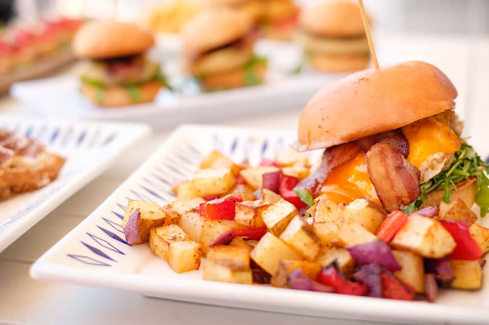 Gourmet burger and crispy potatoes served on white plate with appetizers in background