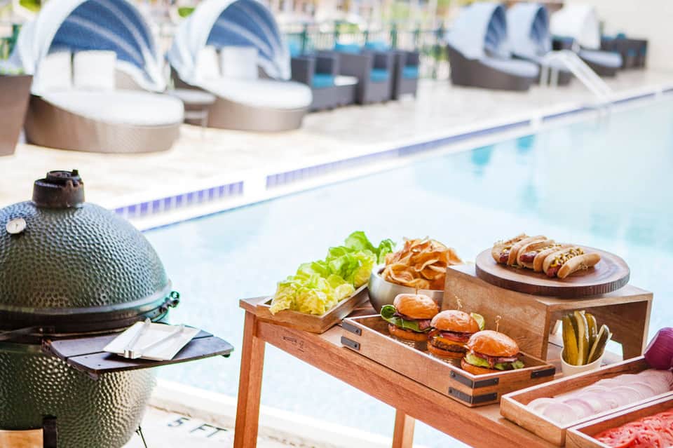Poolside food service with burgers, wraps, and salads on wooden table near resort pool