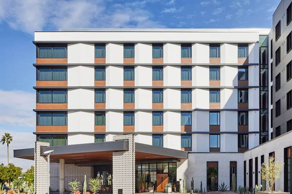 Modern hotel building facade with white and copper striped pattern, large windows, and palm trees