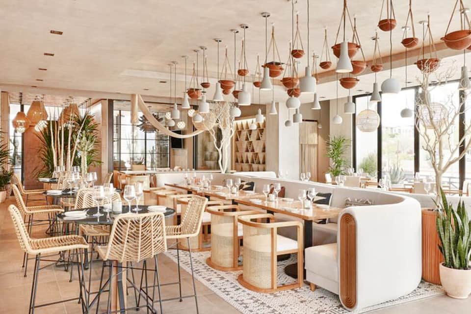 Modern restaurant interior with hanging pendant lights, wooden furniture, and contemporary coastal design