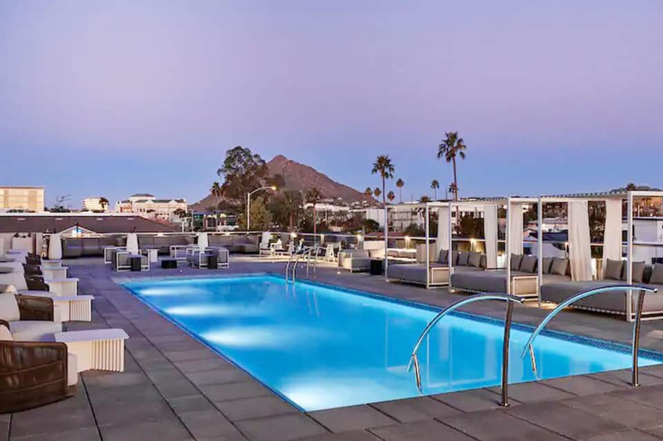 Illuminated resort pool at dusk with lounge chairs and mountain views