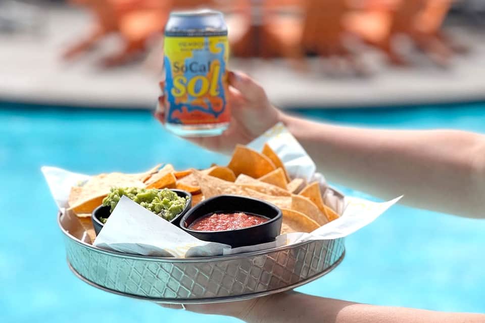 Cold beverage and chip platter with dip served poolside on turquoise water background