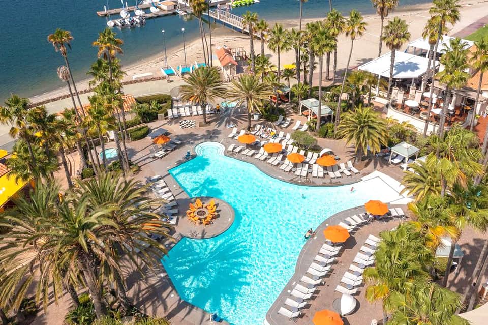 Aerial view of resort pool with orange umbrellas, palm trees, and beach access