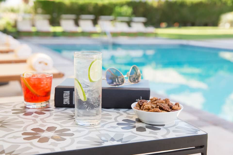 Poolside refreshments with cocktails, sunglasses, and snacks on decorative table